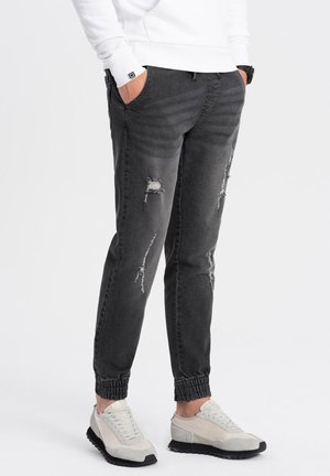Joggers de mezclilla gris con puños elásticos, presentan detalles desgastados y un ajuste holgado, combinados con zapatillas gris claro.