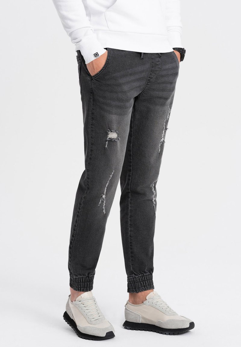 Joggers de mezclilla gris con puños elásticos, presentan detalles desgastados y un ajuste holgado, combinados con zapatillas gris claro.