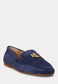 Mocassins de camurça azul-marinho com bico arredondado, emblema de hardware dourado na banda e sola castanha. Textura suave e design clássico.