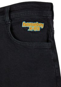 Jeans de mezclilla negra con un logo bordado "homeboy X-tra" en naranja y azul en el bolsillo frontal. Diseño de cinco bolsillos con costuras estándar.