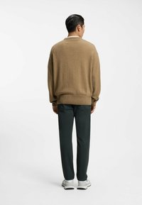 Maglione kaki in tessuto di maglia morbida, vestibilità morbida, polsini e orlo a costine, abbinato a pantaloni verde scuro, completato da scarpe da ginnastica bianche.