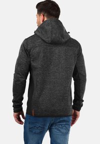 Dark gray hoodie with black accents, textured fabric, adjustable hood, zippered side, and a leather logo patch near the hem.