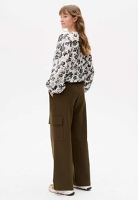 Florale Bluse mit langen, gepufften Ärmeln und Rundhalsausschnitt, kombiniert mit weiten olivgrünen Hosen mit Seitentaschen. Sportliche Schuhe.