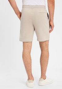 Beige Baumwollmischung-Shorts mit einem Kordelzugbund, Seitentaschen und einer einzelnen Gesäßtasche. Glatte Textur mit entspannter Passform.