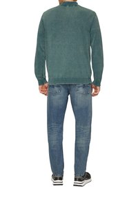 Turquoise gebreide trui met een kraag, lange mouwen, geribbelde manchetten en onderrand, gecombineerd met lichtblauwe denim jeans en zwarte sneakers.