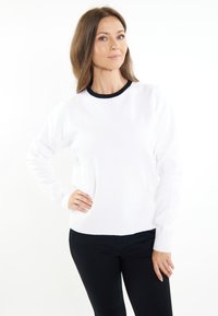 Pulover alb tricotat, cu guler rotund negru, mâneci lungi, manșete și tiv cu nervuri. Purtați peste pantaloni negri.