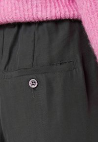 Tmavě šedé kalhoty s hladkou texturou, vybavené přední kapsou a zavíráním na fialový knoflík. Pas je elastický.