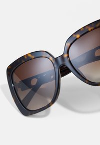 Ochelari de soare din material țestoasă cu rame mari, pătrate, lentile întunecate de culoare maro și balamale vizibile. Textură netedă, design la modă.