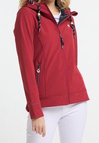 Röd mjukskaljacka med dragkedja, huva och snoddar; har sidofickor med dragkedjor och kontrasterande grå sömmar.