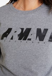 Sudadera de algodón gris con un audaz logo negro "ARMANI EXCHANGE" con un acabado texturizado, cuello redondo y corte holgado.