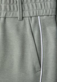 Un pantalon de survêtement vert clair texturé avec une taille élastique et une poche latérale agrémentée d'une bande blanche.