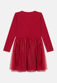 Rdeča obleka z dolgimi rokavi in prilegajočim zgornjim delom, ter svetlečo, plastasto tuljeno krilo. Tulle vsebuje srebrne pikčaste vzorčke, kar ustvarja teksturiran videz.