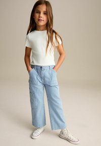 T-shirt blanc à manches courtes en rib et pantalon large rayé bleu clair avec poches latérales et ceinture boutonnée. Baskets blanches.