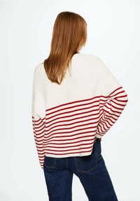 Pull rayé blanc et rouge ; présente une coupe ample avec des manches longues et une texture côtelée. Vue de dos mettant en avant le contraste des couleurs.