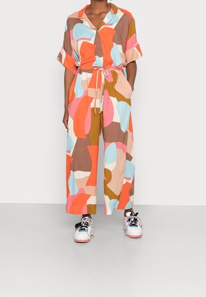 Personne portant une combinaison aux motifs abstraits colorés avec manches courtes et des baskets blanches à lacets multicolores.