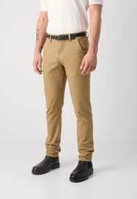 Khaki chinos med rett passform, laget av bomullsblanding. Har sidelommer og et svart lærbelte. Brukt med svarte ankelstøvler.