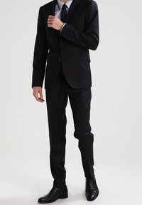 Svart kostym med skräddarsydd passform, bestående av en enkelknäppt kavaj, notch revers och matchande byxor, ihop med svarta läderskor.