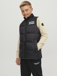 Črn podložen brezrokavnik z visokim ovratnikom, ki nosi logo "JACK & JONES". Obute nad krem puloverjem, v kombinaciji s črnimi trenirko hlačami.