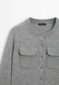 Cardigan en laine gris clair avec col rond, fermeture boutonnée à l'avant et deux poches à rabat boutonnées sur la poitrine.