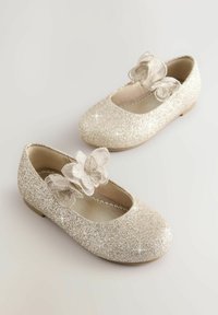 Glittrande guldballerinas med rund tå och genomskinliga blomdekor, med platt sula och slät inredning.