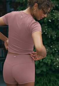 Lühikeste varrukatega sporditop ja lühikesed püksid pehmest mauve materjalist. Omab kehaühendavat disaini, millel on tagasi peen bränding ja sujuv tekstuur.
