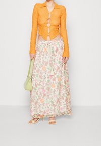 Top corto de encaje naranja con botones y mangas largas, combinado con una falda maxi floral fluida de colores pastel y cintura con cordón.