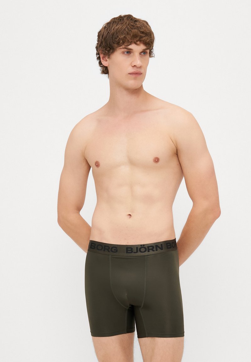 Olīvu zaļas bokseršortus ar melnu elastīgu jostasvietu, kurā ir teksts "BJÖRN". Gluda viela un pieguloša forma.