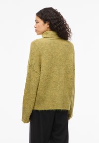 Camisola de malha verde com gola alta, corte solto e barra canelada. Textura suave, design oversized e detalhes mínimos nas costas.