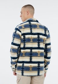 Fleece shirt met een geometrisch patroon in marineblauw, roomwit en tan. Heeft lange mouwen en een kraag, met een ontspannen pasvorm en een zachte textuur.