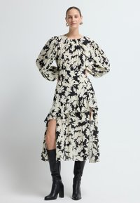 Vestido de estampado floral en crema y negro, con mangas abullonadas, una falda de capas con cortes, y se combina con botas negras hasta la rodilla.