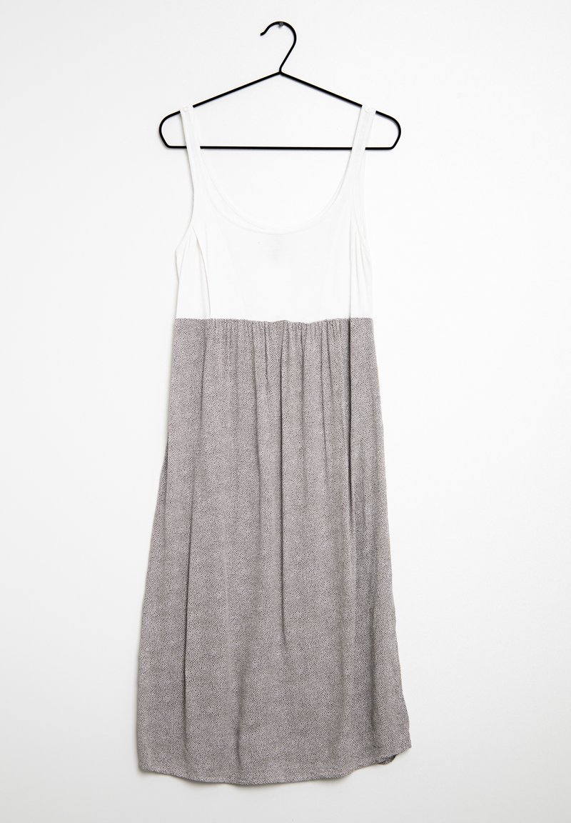 Robe sans manches suspendue sur un cintre noir avec un haut blanc ajusté et une jupe grise ample avec un petit motif à pois.