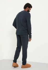 Marineblaues Strick-Loungewear-Set mit einem langärmligen Crewneck-Oberteil und tapered Hosen. Mit gerippten Bündchen und lockerer Passform. Hausschuhe im Wildleder-Look.