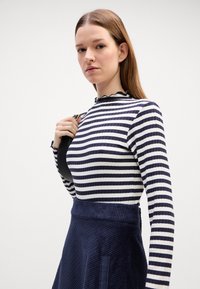 Marineblau und weiße gestreifte langärmelige Bluse mit Rüschenausschnitt, kombiniert mit einem strukturierten marineblauen Cordrock mit breitem Bund.