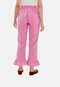 Růžové kostkované kalhoty s rozšířeným lemem a elastickým pasem. Tkanina má kostkovaný vzor a nohavice mají na konci mírně řasený lem.