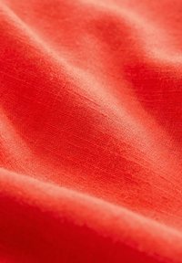 Primer plano de una tela roja, con una textura suave y un sutil patrón de tejido. El material parece ligero y suave, mostrando una profundidad de color vibrante.