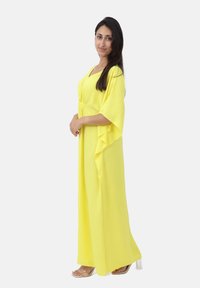 Robe maxi jaune avec manches kimono, tissu texturé et taille cintrée, assortie à des sandales à talons blocs transparents.