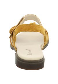 Yellow suede sandals with a flat sole, featuring a bow accent and adjustable straps. The insole is light-colored with a brand logo.