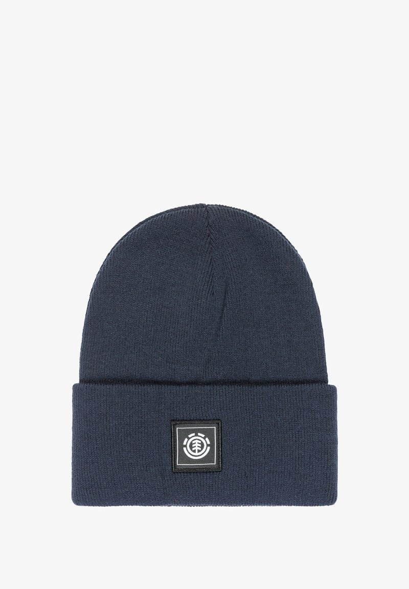 Navy blue knit beanie with a rolled cuff and a square black patch featuring a circular logo. Made of soft, textured fabric.