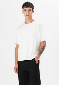 Hvid bomulds T-shirt med rund hals, dropped skuldre og en afslappet pasform. Bæres med sorte cargo bukser.