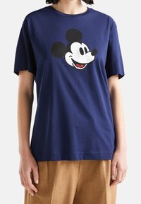 Námořnicky modré bavlněné tričko s velkým grafickým vyobrazením obličeje Mickeyho Mouse v černé, bílé a červené barvě. Krátké rukávy, volnější střih.