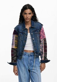 Denim jacket with colorful embroidered fabric sleeves, featuring various patterns. Button-up front and classic collar design.