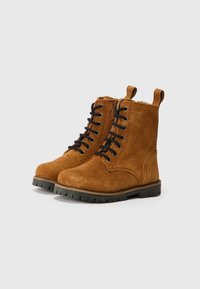 Bruna mockaskinnankelboots med svarta snören, rund tå och texturerad gummisula. Har en dragflik bak och sömnadsdetaljer.