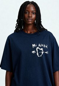 T-shirt en coton bleu marine surdimensionné avec inscription blanche "Mi Amor" et dessin de cœur avec des flèches. Manches courtes et encolure ras du cou.
