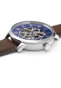 Montre squelette avec un cadran bleu, des chiffres romains et un boîtier en acier inoxydable argenté. Équipée d'un bracelet en cuir marron et de mécanismes internes visibles.