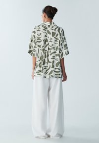 Camicia a maniche corte,ampia e comoda, con un motivo astratto verde su uno sfondo chiaro; abbinata a pantaloni bianchi larghi.