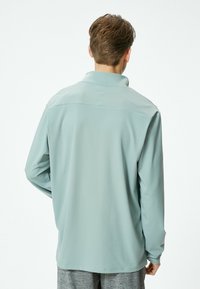 Camisa de manga larga azul claro con alto cuello, hecha de tejido suave. Presenta un diseño limpio con costuras mínimas y un ajuste relajado.