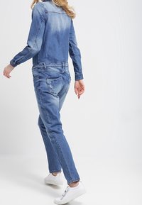 Jeansjacka med blekt blå gradient, långa ärmar och framfickor, tillsammans med ljusblå jeans och vita sneakers.