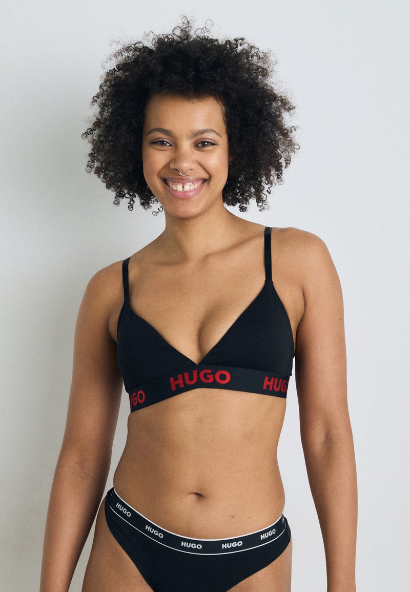 Zwarte bh met een V-halsontwerp en dunne bandjes, voorzien van een rode "HUGO" logo band. Bijpassende zwarte bikini met een witte "HUGO" tailleband.