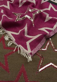 Écharpe tissée magenta avec des motifs d'étoiles blanches et des sequins, bords frangés, présentée sur une base brune texturée avec des accents d'étoiles rouges.