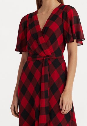 Robe portefeuille à carreaux rouges et noirs avec manches courtes volantées et ceinture nouée à la taille sur une personne debout.